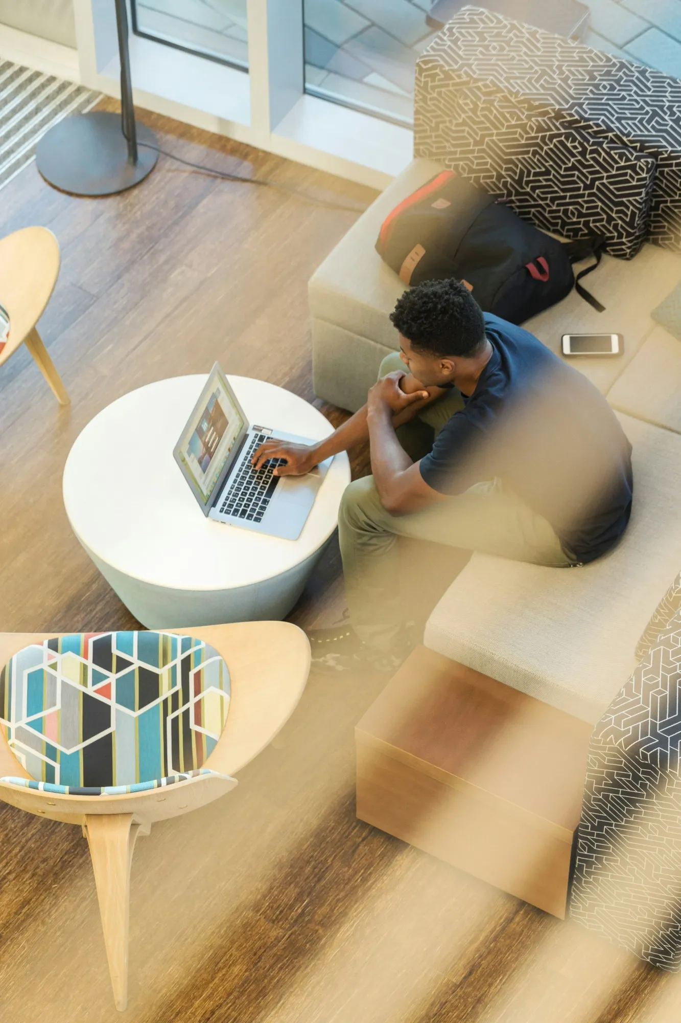 A person working on a laptop at a low table in a bright lounge, seen from above