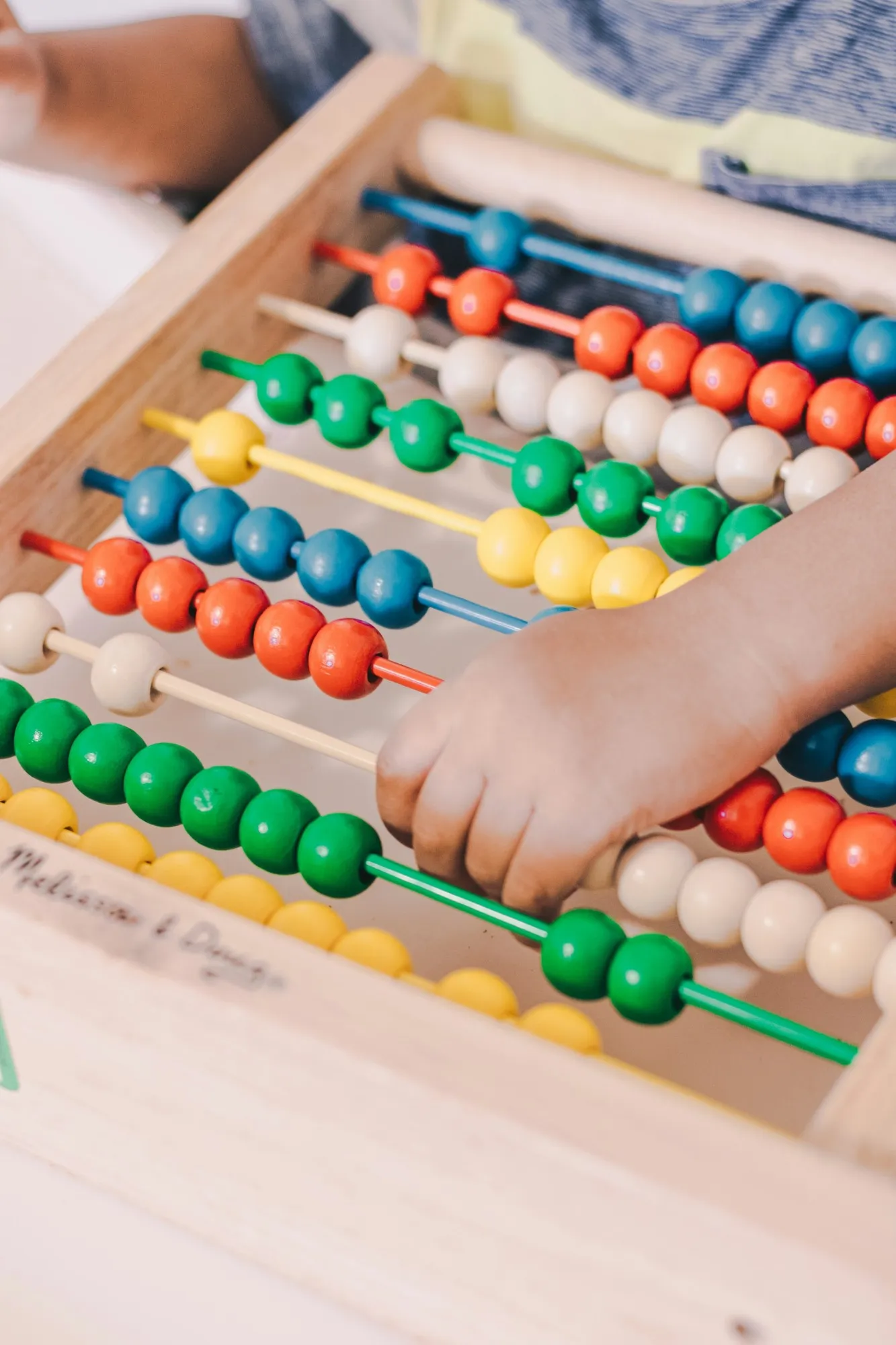 A child's hand moving coloured beads on a wooden abacus