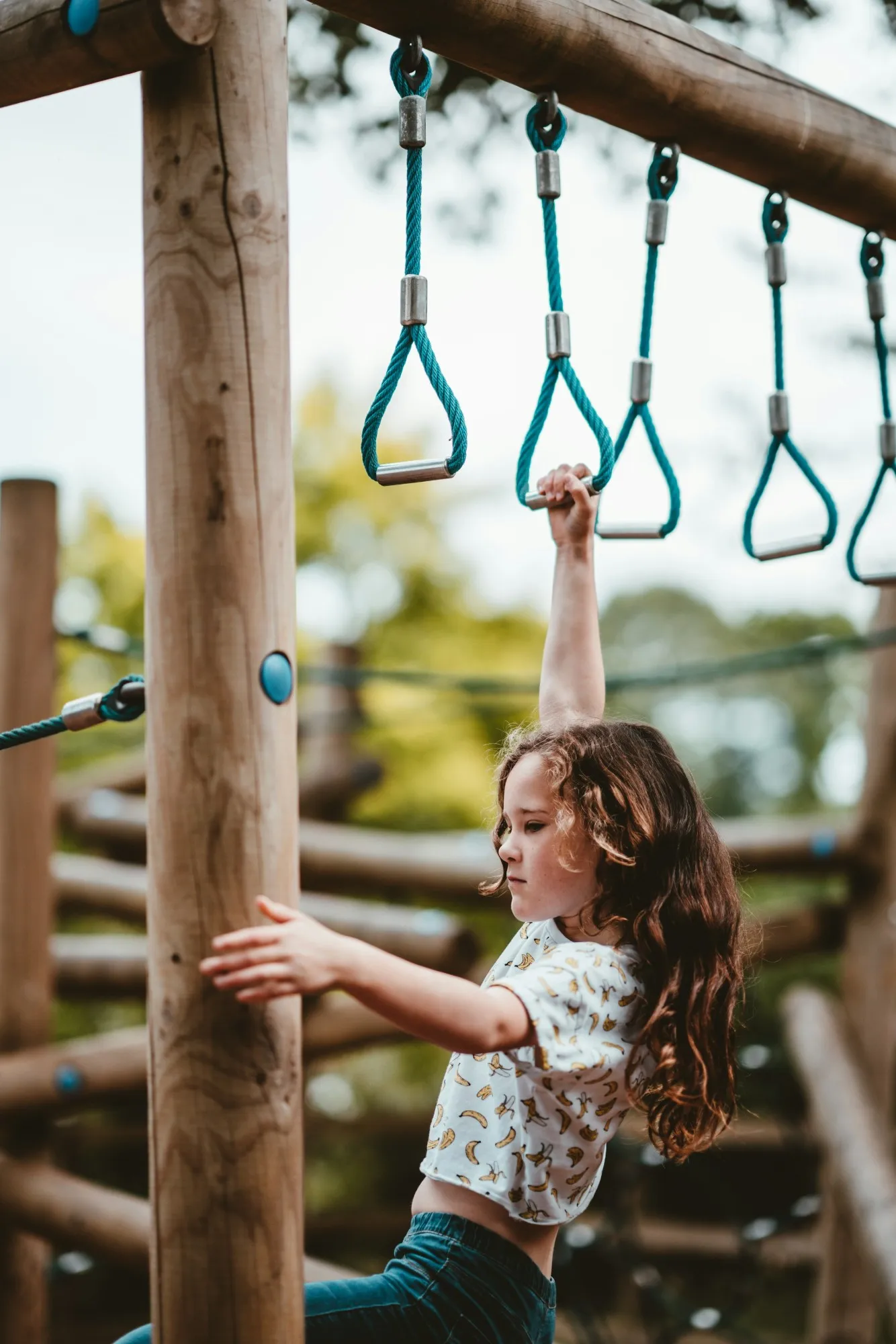 A child hanging from a set of rope rings on a wooden playground